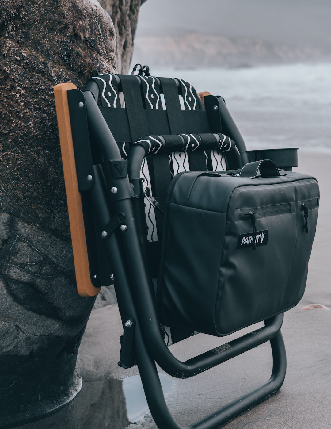 Voyager outdoor chair in slate folded and leaning against a rock on the beach in Big Sur